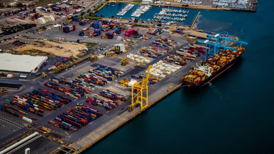 Aerial view of a port showing container terminals, quay cranes, a vessel alongside and the surrounding land